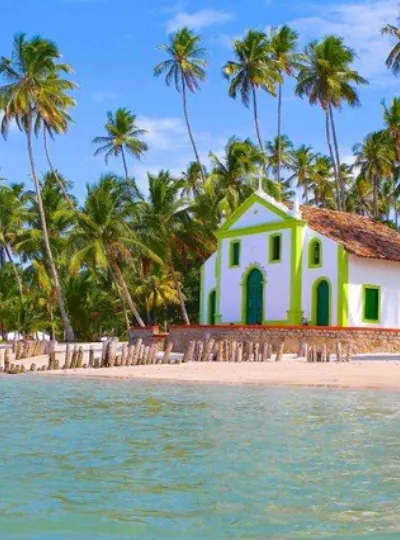 Capela branca entre coqueiros, à beira da praia